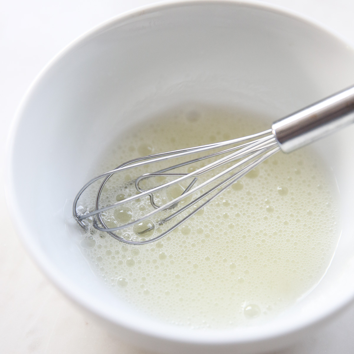 Frothy egg whites in a bowl with a whisk