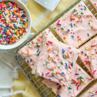 sugar cookie bars with pink frosting stacked on a tray