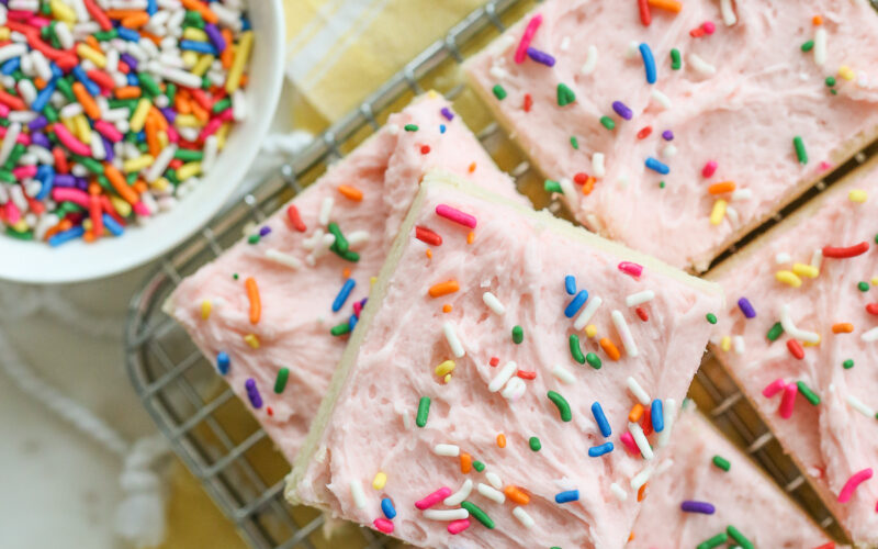 sugar cookie bars with pink frosting stacked on a tray
