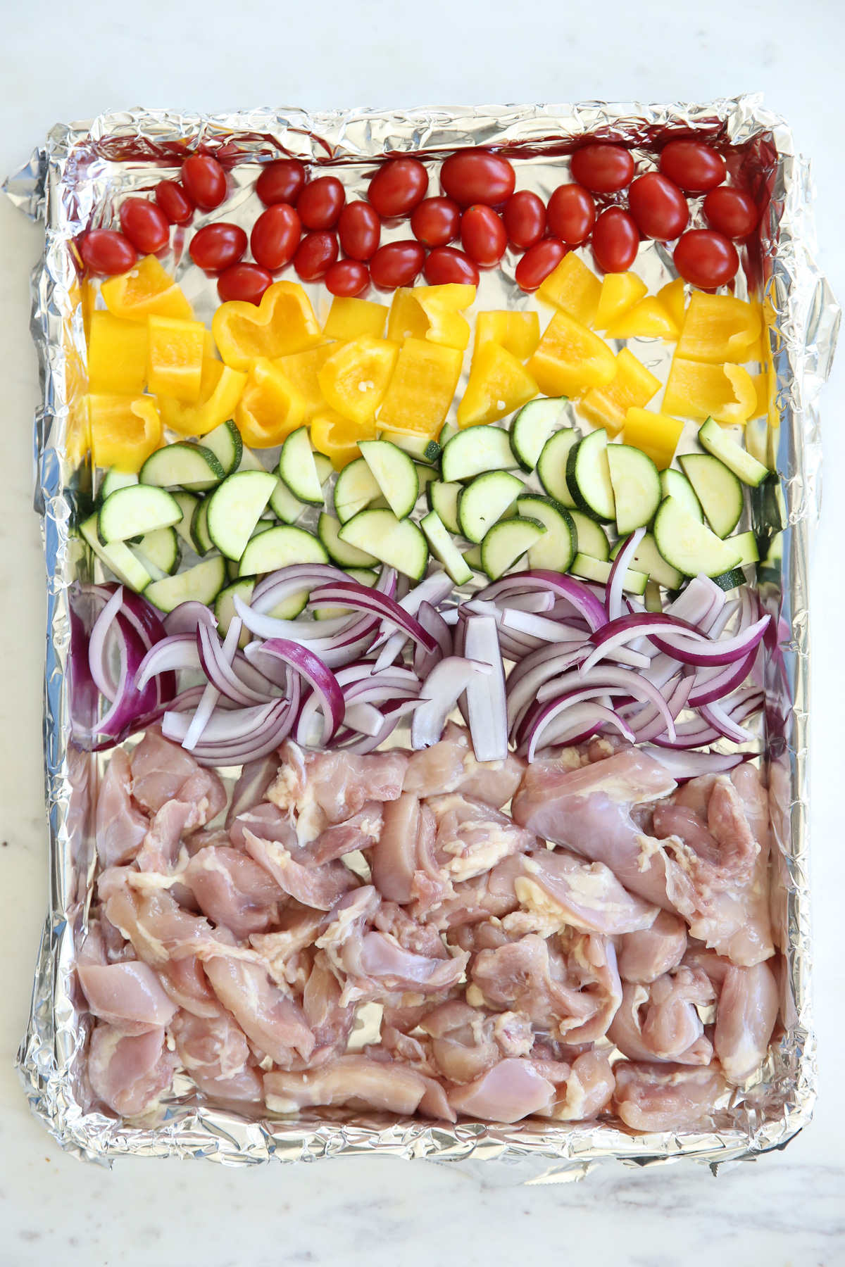 raw chicken and vegetables on a sheet pan