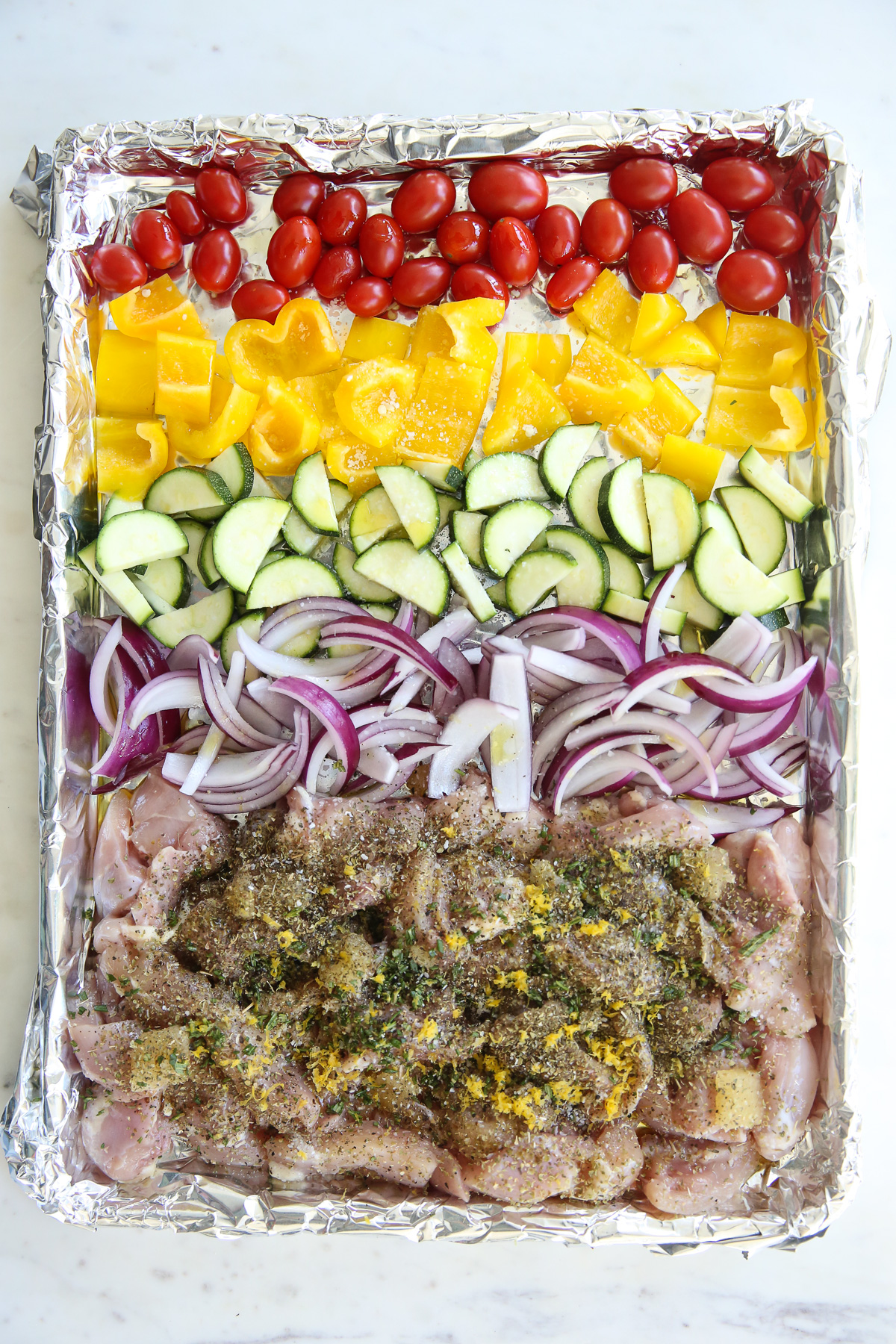 raw chicken and vegetables on a sheet pan