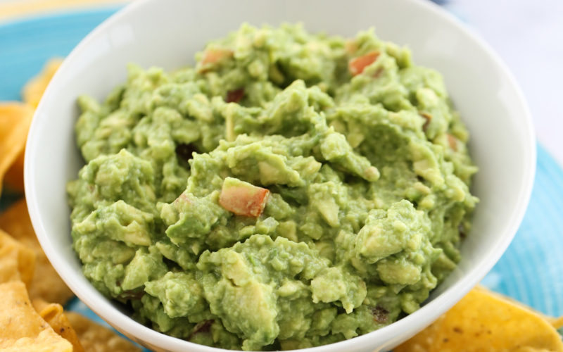 guacamole in a white bowl surrounded by chips