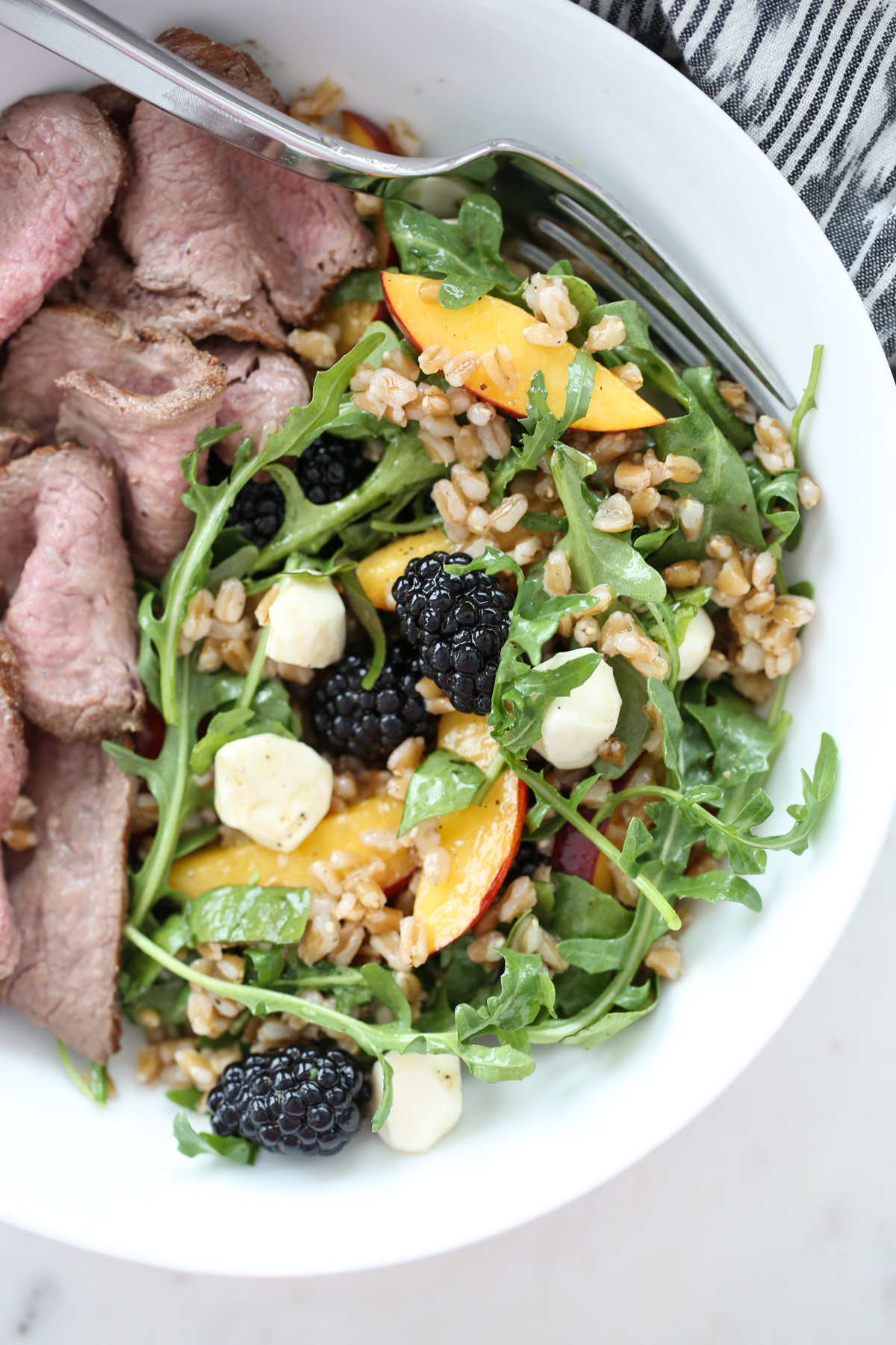 peach arugula salad in a white bowl with sliced steak