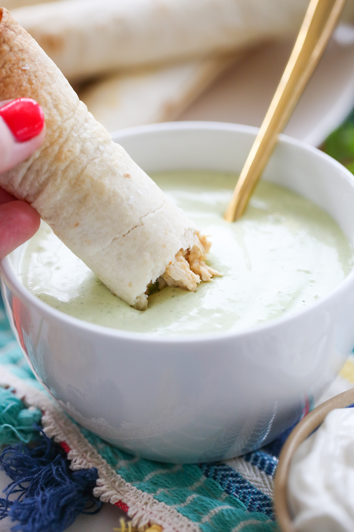 baked taquitos dipping in green sauce